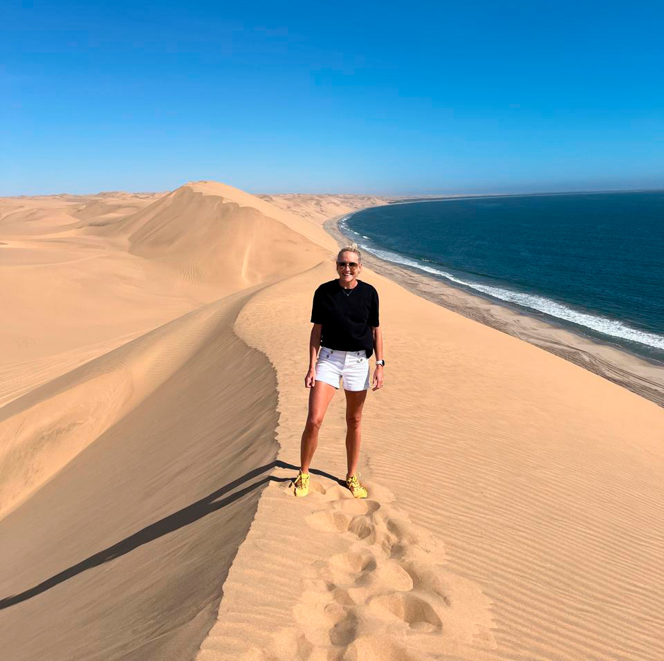 Camille Rowe standing on the dunes above the Atlantic Ocean at Sandwich Harbour in Namibia.